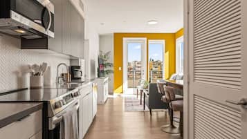 Une cuisine moderne équipée d’un four à micro-ondes, d’une cuisinière et d’un évier. On y trouve également un coin repas avec une table et des chaises. La pièce offre une vue sur la ville.