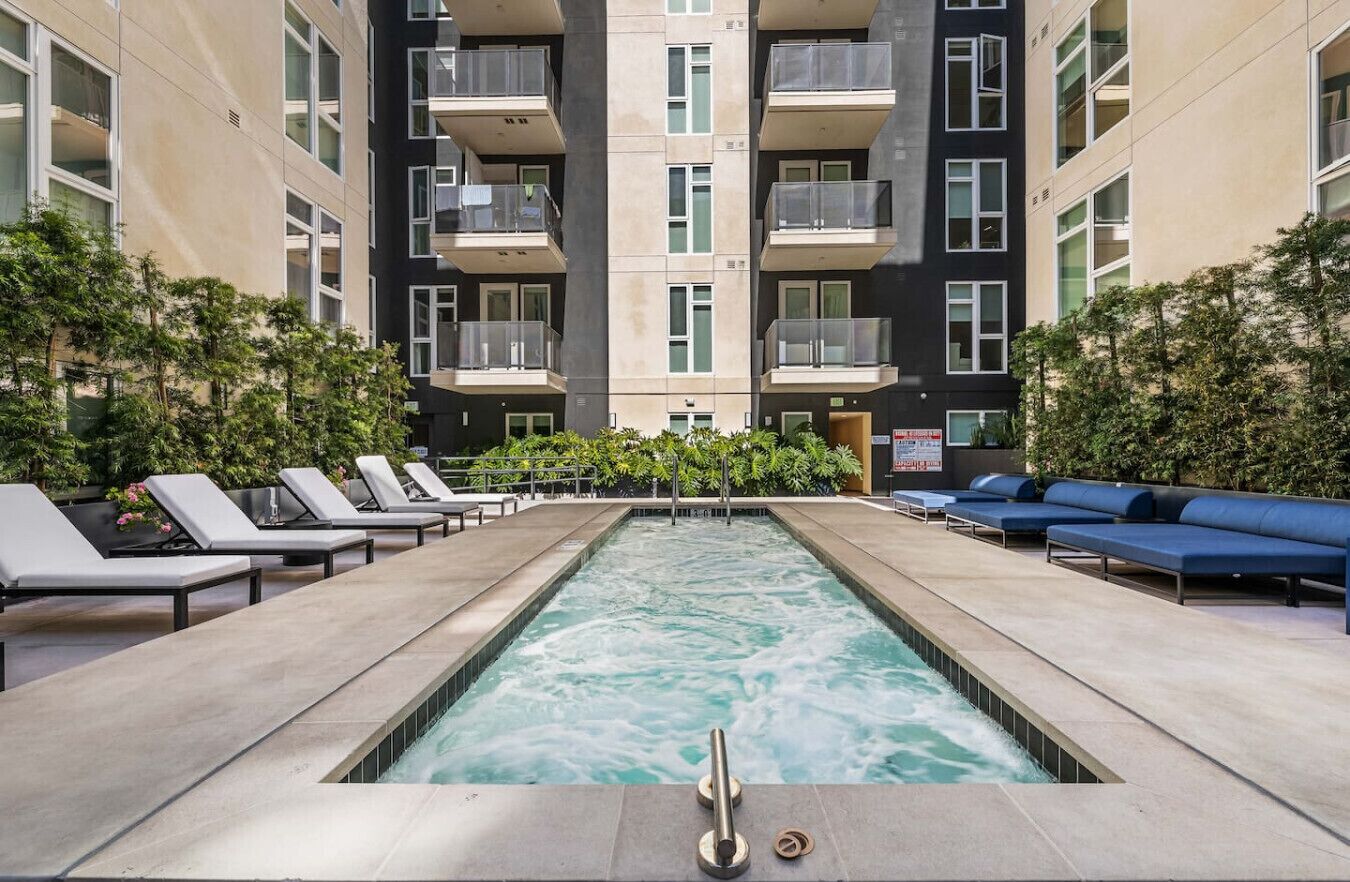 A swimming pool with lounge chairs and a blue sofa, surrounded by a building with balconies.