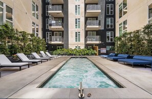 A swimming pool with lounge chairs and a blue sofa, surrounded by a building with balconies. - Bright & Chic 2BDR Suite K-Town Haven, Hot tub + Gym (Los Angeles)