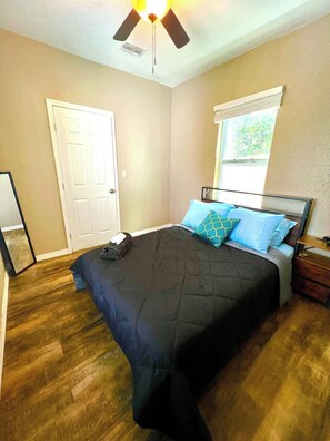 Un dormitorio con cama, ventana con persianas, puerta y ventilador de techo.