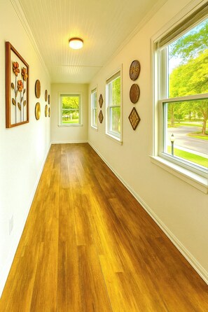 A hallway with wooden flooring, multiple windows, and wall-mounted decorative items. - Massive on Myrtle St - 7 mins from DT - Sleeps 15 (Jacksonville)