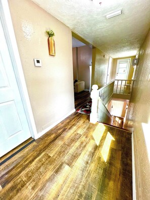 Un pasillo con piso de madera, una puerta blanca y una escalera que conduce a un nivel superior.