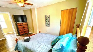 A bedroom with a bed, wooden headboard, a ceiling fan, a dresser, and a television.