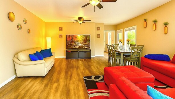 A living room with a sofa, a red couch, a dining table with chairs, and a ceiling fan.
