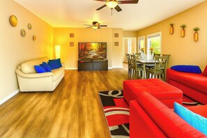 A living room with a sofa, a red couch, a dining table with chairs, and a ceiling fan. - Massive on Myrtle St - 7 mins from DT - Sleeps 15 (Jacksonville)