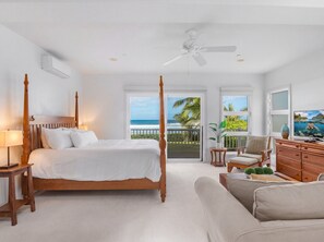 Een slaapkamer met hemelbed, plafondventilator, uitzicht op de oceaan en een balkon met uitzicht op palmbomen.
