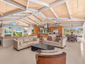 Un área de estar amplia con techo alto, ventanas grandes y una cocina moderna.