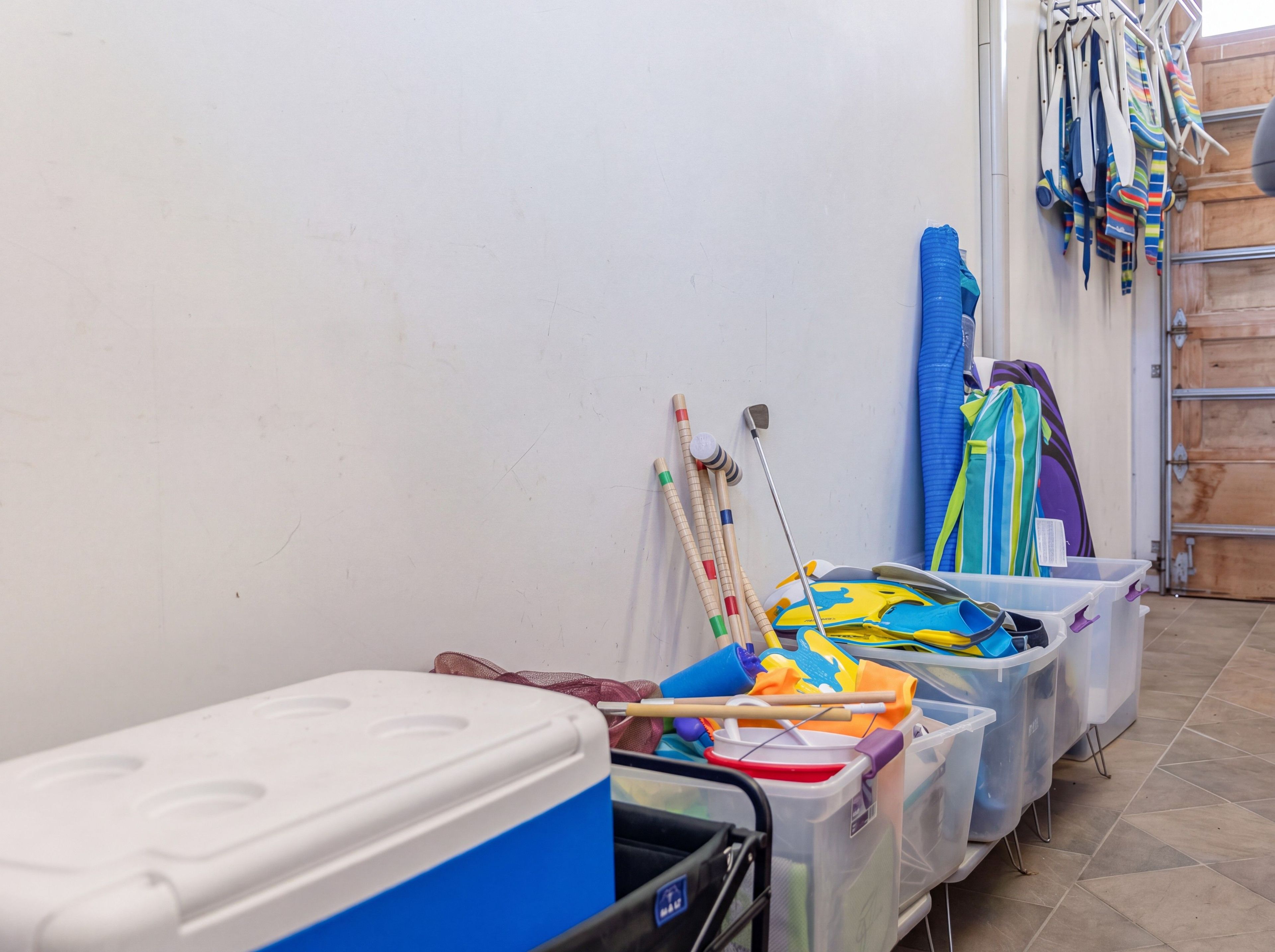Un espace de rangement avec des bacs en plastique contenant divers objets, une glacière blanche et un présentoir avec des articles aux couleurs vives.