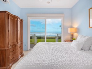 A bedroom with a large bed, a wooden wardrobe, a nightstand with a lamp, and a view of the ocean through a sliding door. - Beachfront North Shore Oahu Estate | Sunset Beach (Haleiwa)