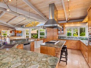 A spacious kitchen with granite countertops, wooden cabinets, and a large island. - Beachfront North Shore Oahu Estate | Sunset Beach (Haleiwa)