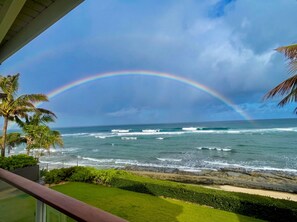 Een uitzicht op de oceaan met golven, een regenboog en palmbomen.