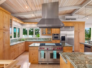 A modern kitchen with wooden cabinets, a stainless steel range, and a large island with a built-in oven. - Beachfront North Shore Oahu Estate | Sunset Beach (Haleiwa)