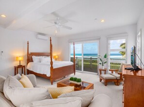 A bedroom with a four-poster bed, a balcony with a view of the ocean, a television, and a seating area with a coffee table. - Beachfront North Shore Oahu Estate | Sunset Beach (Haleiwa)
