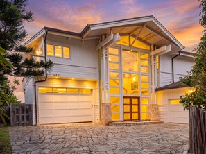 A two-story house with a stone-paved driveway, a garage, and a large glass entry door. - Beachfront North Shore Oahu Estate | Sunset Beach (Haleiwa)