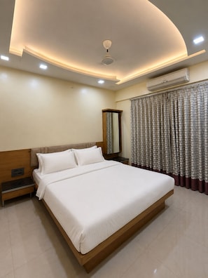 Una habitación de hotel moderna con una cama grande, una mesita de noche, un espejo, un equipo de aire acondicionado e iluminación empotrada en el techo.