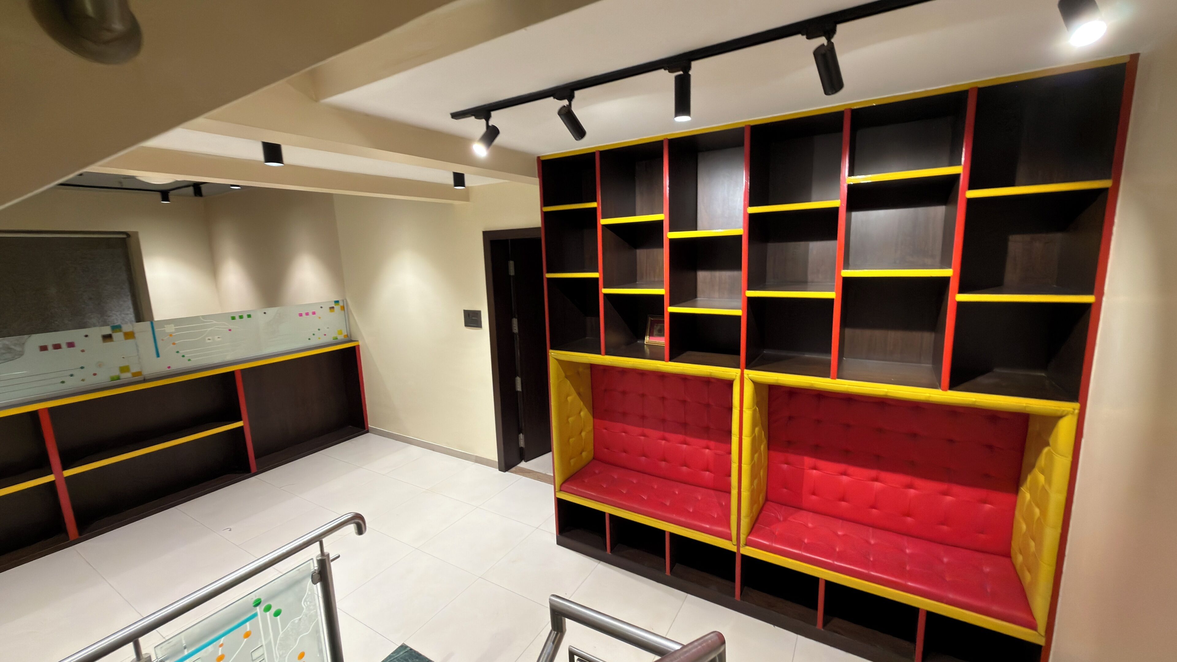 Un interior moderno con una zona de estar que presenta bancos tapizados en rojo y amarillo, una pizarra con marcadores de colores, e iluminación empotrada en el techo.