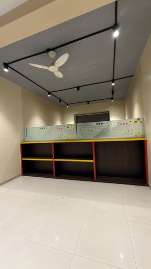 Una habitación con ventilador de techo, iluminación empotrada, una pizarra con marcas de colores y un escritorio con estantes.