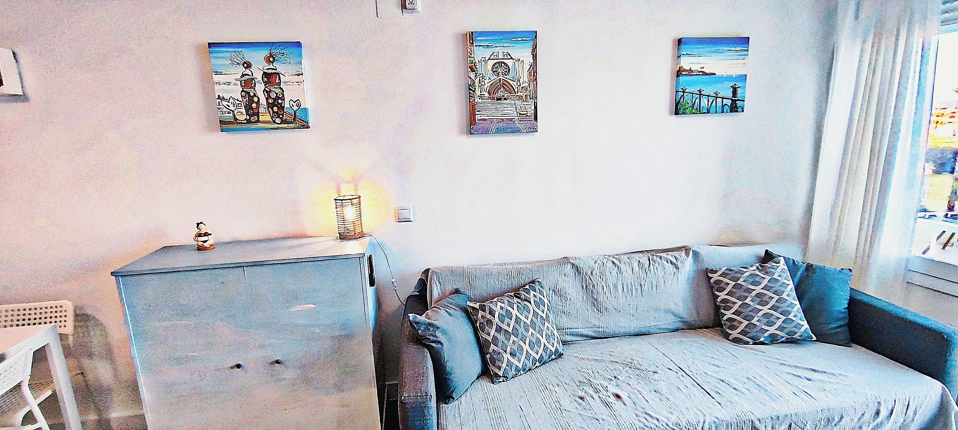 A living room with a sofa, a small cabinet, and three wall-mounted pictures.