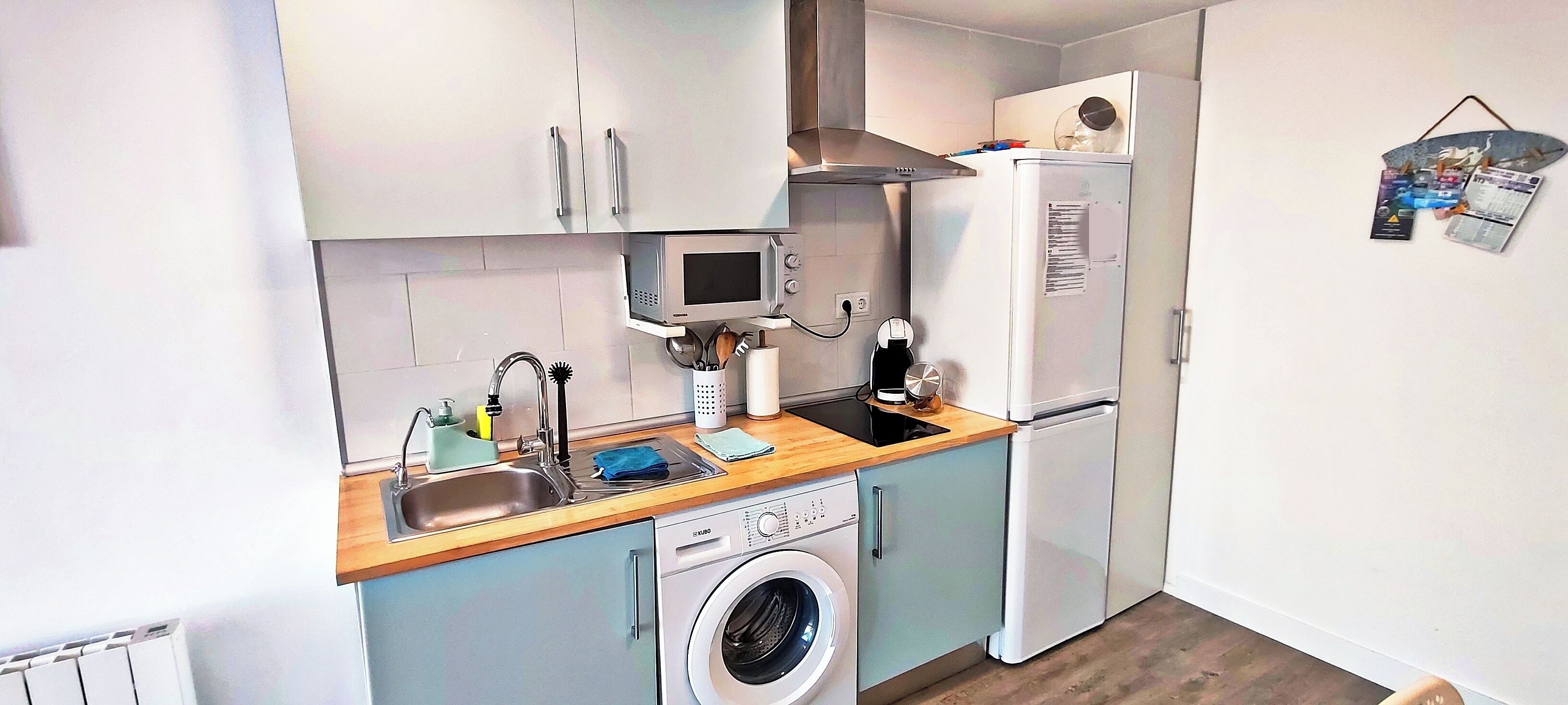 A compact kitchen with a washing machine, a microwave, and a refrigerator.