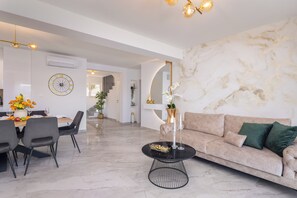 A modern living room with a marble floor, a round coffee table, a sofa with green cushions, and a dining area with a large wall clock. - Luxury seaside Villa Porat with pool, sauna and sea view in Kanica-Rogoznica (Rogoznica)