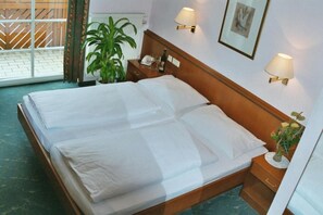 A hotel room with a double bed, bedside tables, a potted plant, a framed picture on the wall, and a window with a view. - Radhotel Schischek (Halbenrain)