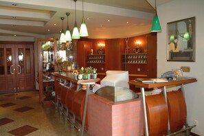 A bar area with a brick counter, hanging green pendant lights, and a wall with shelves displaying various items. - Radhotel Schischek (Halbenrain)