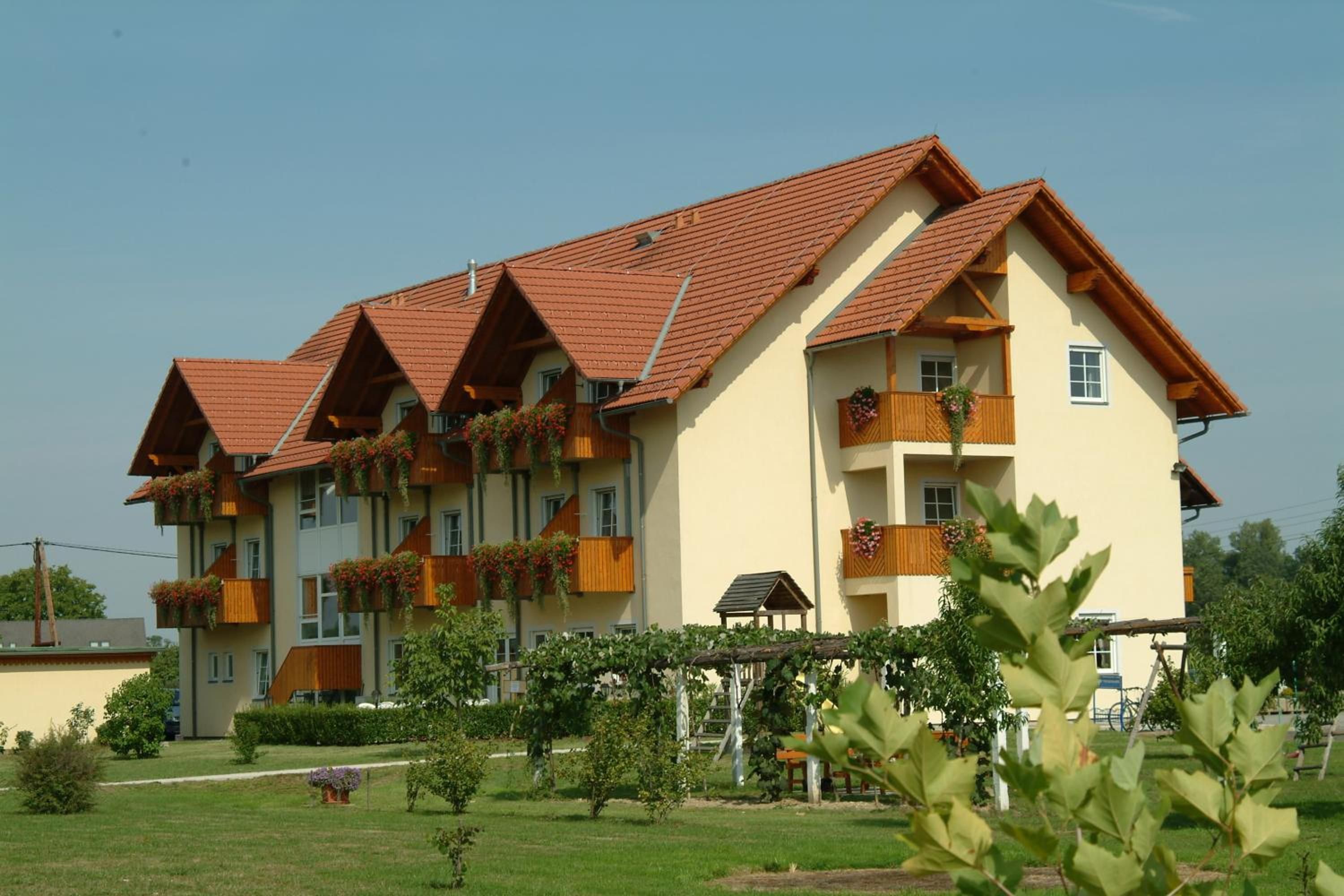 Un hôtel à plusieurs étages, doté d’un toit recouvert de tuiles rouges, de balcons avec des garde-corps en bois et d’un jardin bien entretenu.