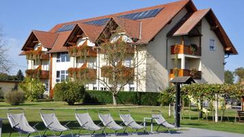 Ein Hotel mit Schwimmbad, mehreren Balkonen und einem Gartenbereich mit Liegestühlen.