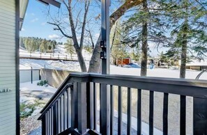 Eine Holzterrasse mit Geländer, mit Blick auf eine verschneite Landschaft mit Bäumen und blauem Himmel.