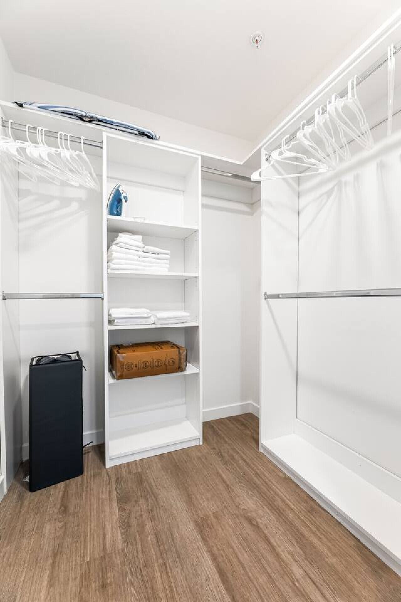 A walk-in closet with open shelves, a hanging rod, and a suitcase on the floor.