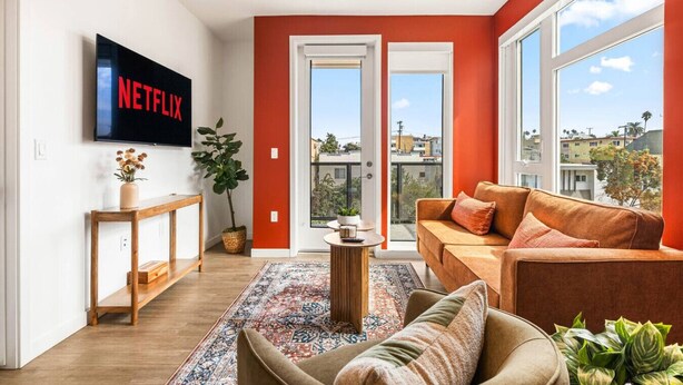 A modern living room with a large TV screen, a sofa, a coffee table, and a view of the city through large windows. - Chic 2 room suite in K-Town, Free Parking, Hot tub + Gym (Los Angeles)