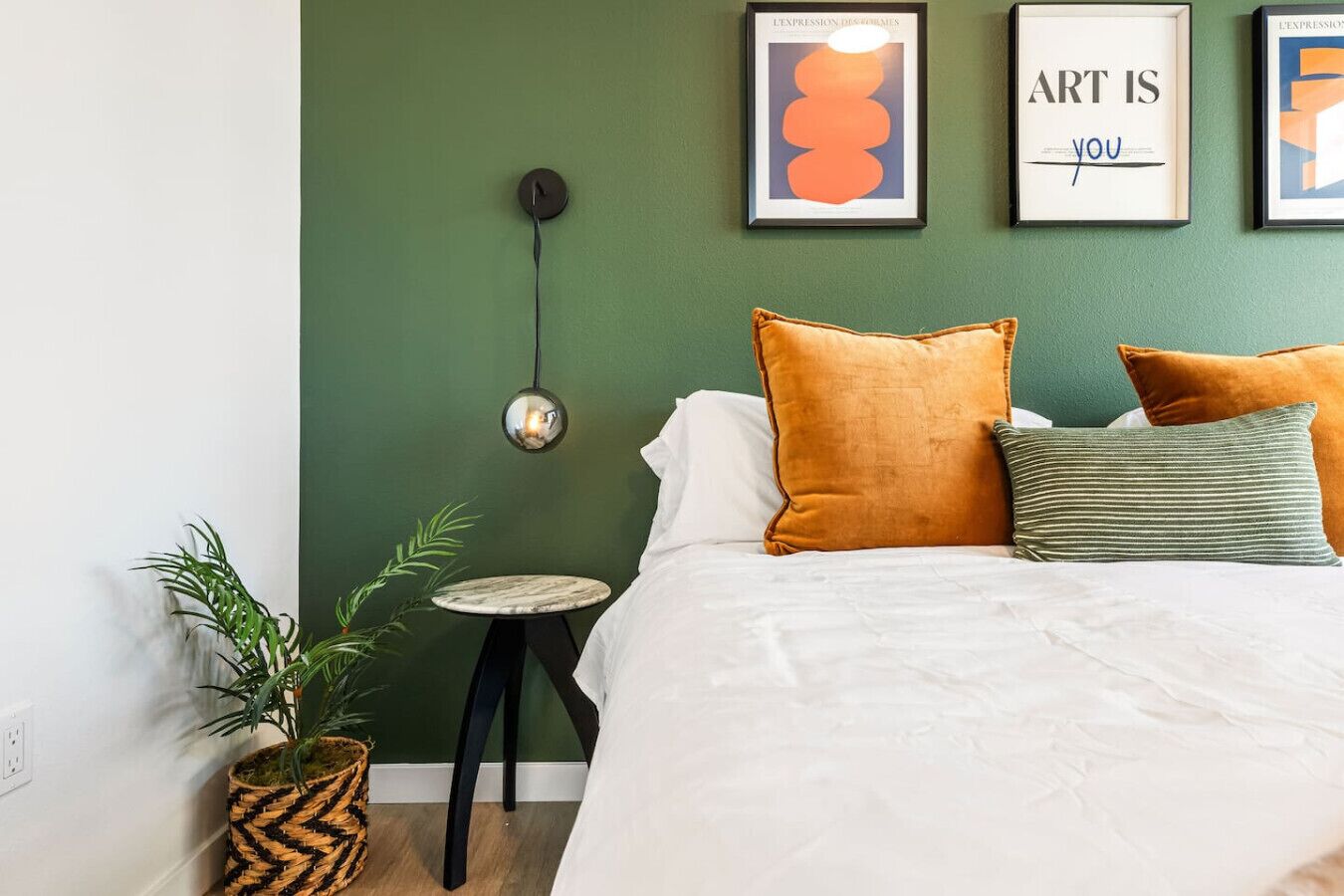 A bedroom with a green wall, a bed with white bedding, and three framed artworks.