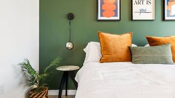 A bedroom with a green wall, a bed with white bedding, and three framed artworks.