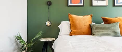 A bedroom with a green wall, a bed with white bedding, and three framed artworks.