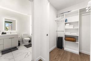 Ett modernt badrum med toalett, handfat och en rymlig klädkammare med hyllor och plats för att hänga kläder.