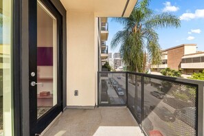 A balcony with a view of a street and buildings, a door leading to a room, and a mesh railing. - Chic 2 room suite in K-Town, Free Parking, Hot tub + Gym (Los Angeles)