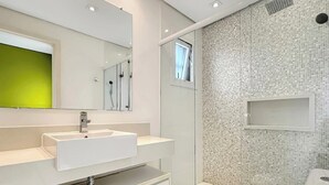 Casa de banho moderna com lavatório branco, espelho e área de duche.