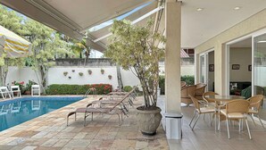 Uma área de piscina externa com espreguiçadeiras, um vaso de plantas e uma mesa de jantar com cadeiras.