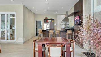 A modern kitchen with a dining area, featuring a wooden table and chairs, a built-in oven, and a large window.