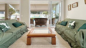Uma sala de estar com dois sofás verdes, uma mesa de centro de madeira e uma cadeira de vime.