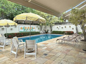Zona de piscina con sillones de descanso y sombrillas a rayas.