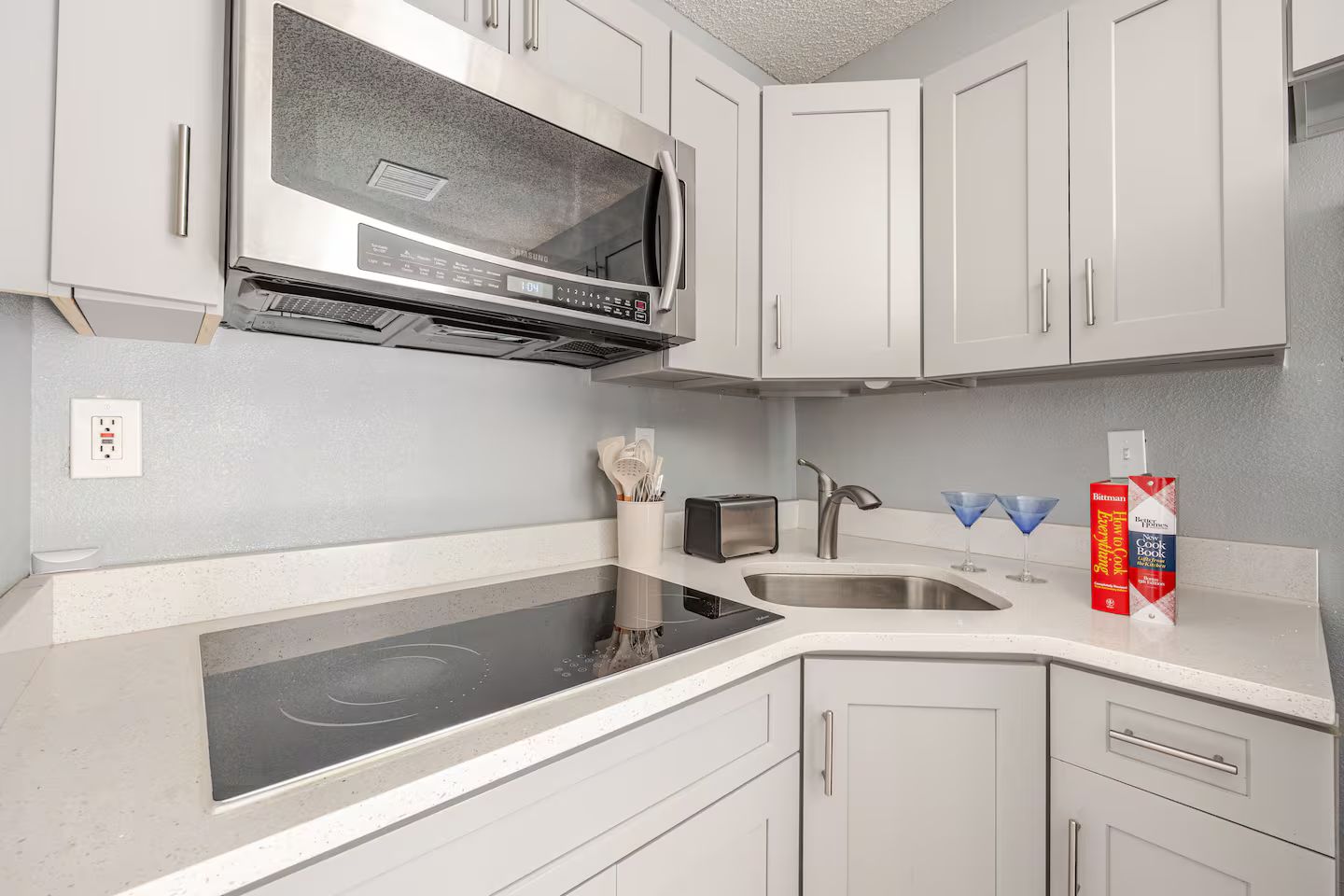 Une cuisine moderne avec des meubles blancs, un four à micro-ondes en acier inoxydable, une plaque de cuisson à induction, un évier et un grille-pain.