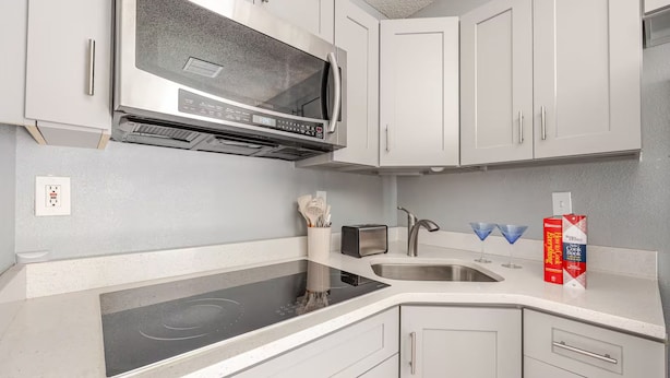 A modern kitchen with white cabinetry, a stainless steel microwave, an induction cooktop, a sink, and a toaster.