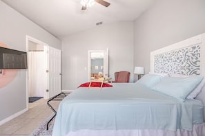 A bedroom with a bed, a chair, a desk, and a mirror.