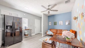 A modern kitchen with a refrigerator, a dining area with a table and chairs, and a living room with a sofa.
