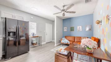 A modern kitchen with a built-in refrigerator, a dining area with a wooden table and chairs, and a living room with a sofa and decorative wall art.