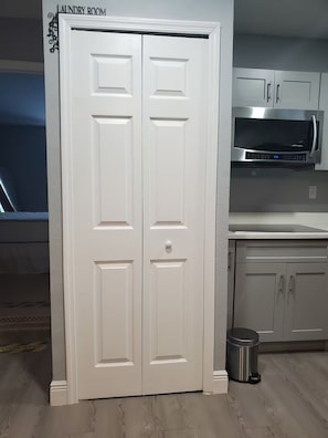 A laundry room with a double door, a microwave, and a trash can.