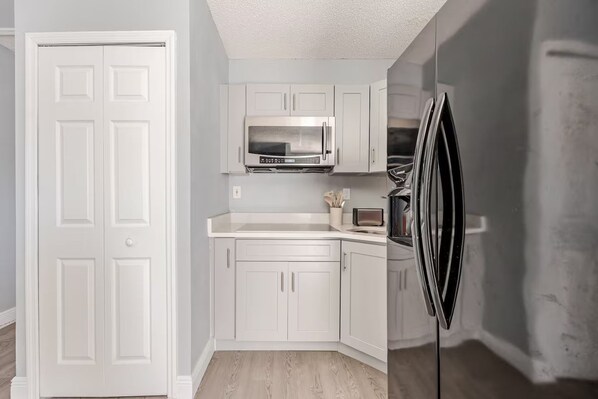 A kitchen with white cabinetry, a microwave, a toaster, and a refrigerator.