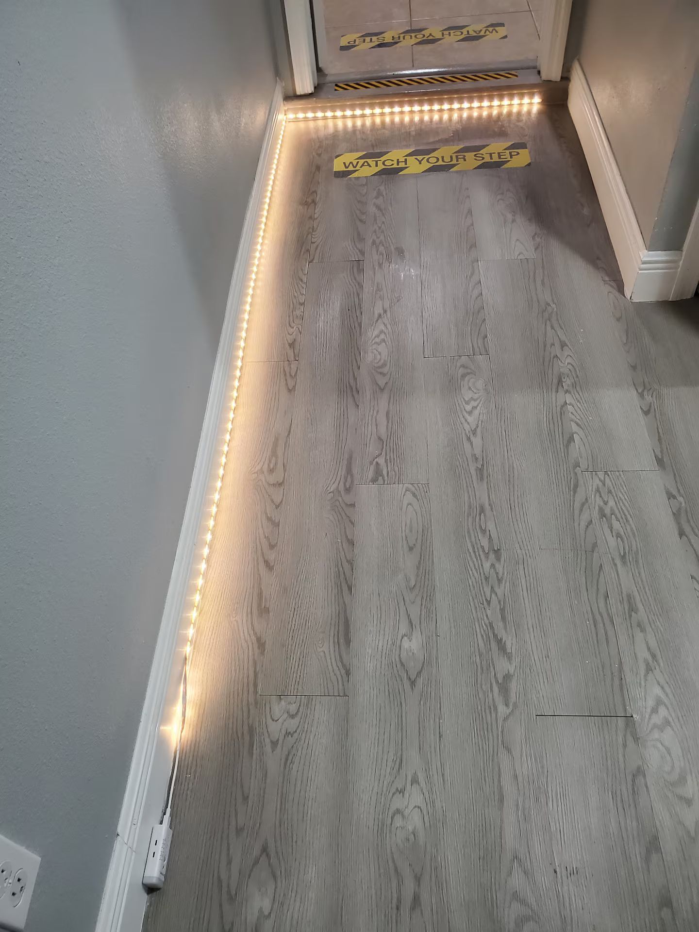 Un plancher en bois avec une bande de lumières le long du plinthe et un panneau d’avertissement sur le sol.