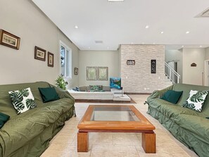 Una sala de estar moderna con dos sofás verdes, una mesa de centro con cubierta de vidrio y una pared de acento de piedra.